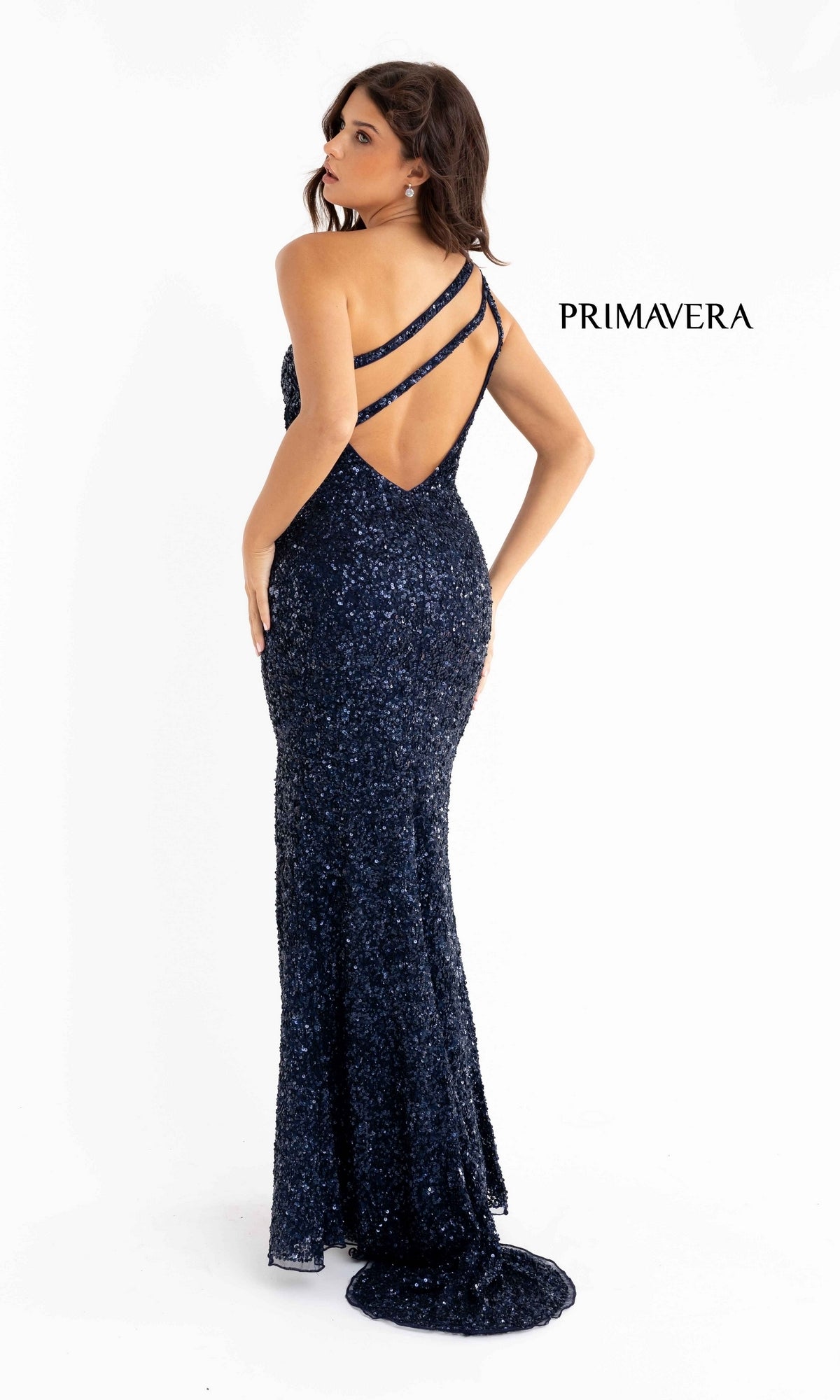 A woman poses in the Strappy-Back Long Sequin Primavera 3761 Prom Dress, a floor-length dark blue gown with double crisscross straps and an open back, against a white background.